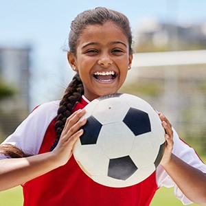 Child smiling while holding soccer ball on field