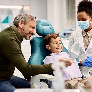 Child with parent and dentist smiling while looking in mirror