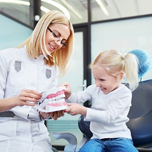 Smiling dentist and child looking at model of teeth