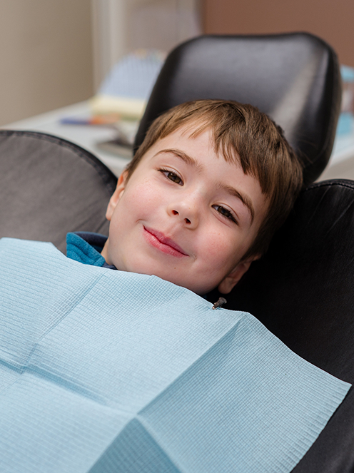 A young boy sitting in a dental chair, preparing for a dental examination in a clinical setting.