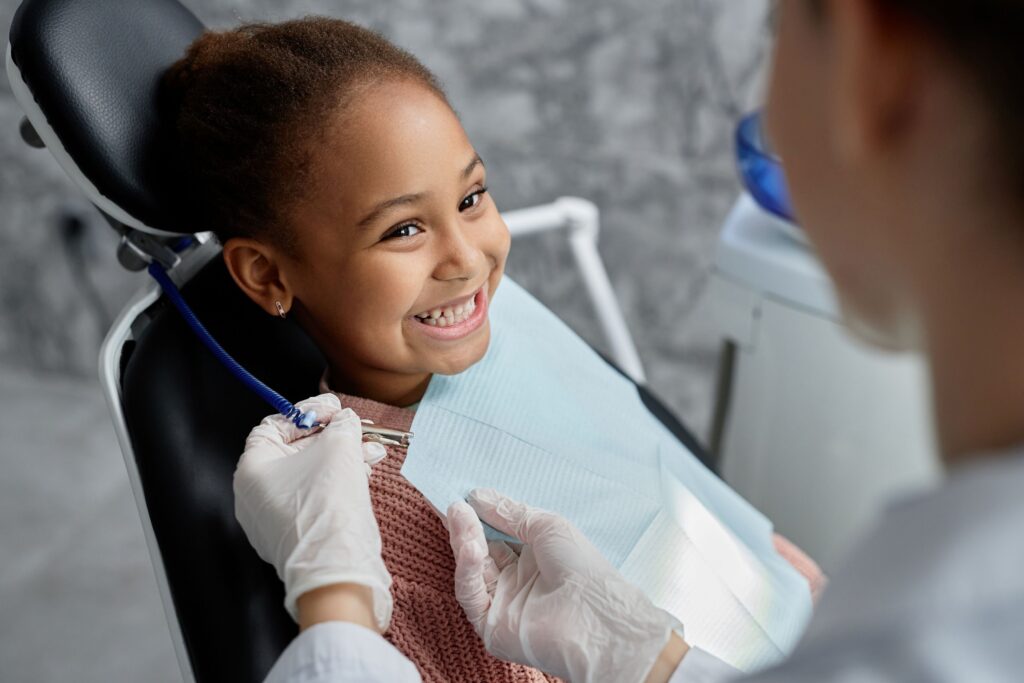 Little girl in dental chair smiling and dentist